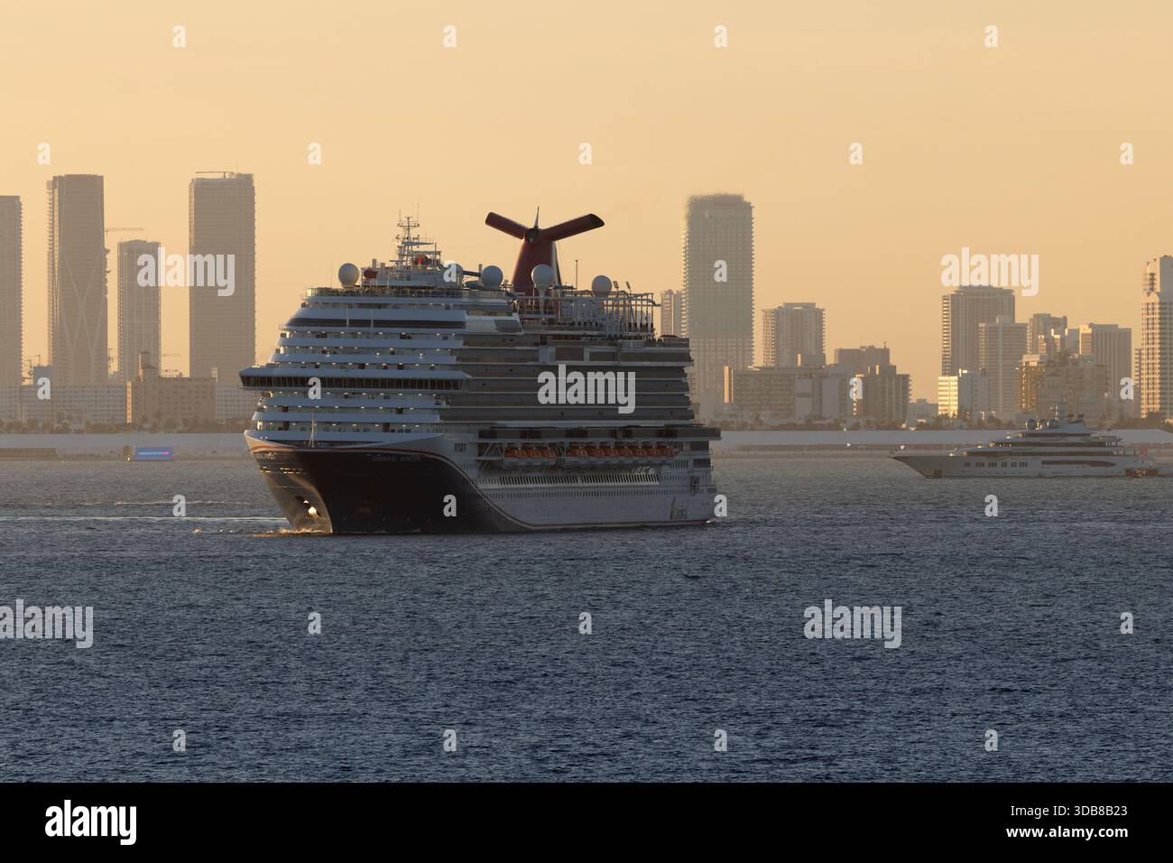 Un grand bateau de croisière Carnival quitte le port de Miami au coucher du soleil, en passant par les gratte-ciel de la ville à travers Biscayne Bay. Banque D'Images