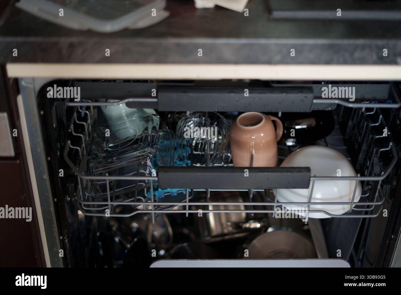 lave-vaisselle ouvert avec vaisselle propre assortie, dont verrerie transparente, céramique beige et blanche, reflétant le cadre de la cuisine avec moderne, muet Banque D'Images
