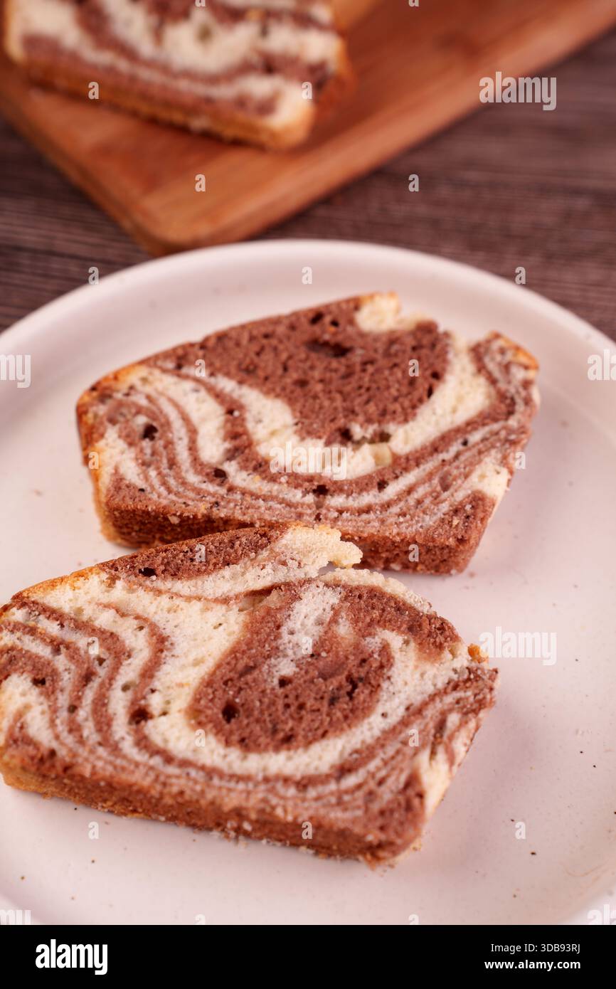 gros plan de gâteau de marbre tranché sur une assiette blanche présentant des tourbillons complexes de chocolat et de vanille avec une planche à découper en bois en arrière-plan, creat Banque D'Images