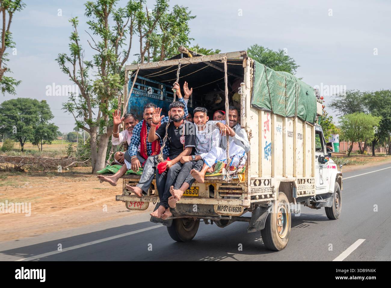 Jeunes hommes à dos d'un camion ouvert sur une route rurale en Inde. Banque D'Images