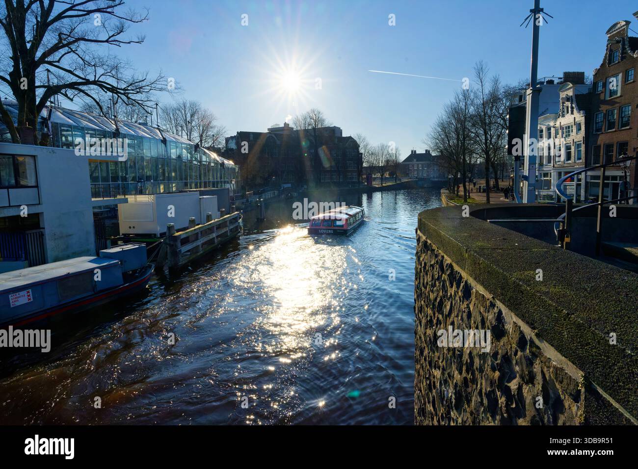 Un après-midi tranquille à Amsterdam comprend un bateau naviguant le long d'un canal, avec la lumière du soleil scintillante sur la surface de l'eau. Les bâtiments voisins créent un pois Banque D'Images