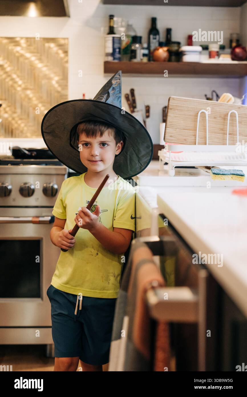 Garçon jouant au sorcier dans la cuisine tenant la baguette magique Banque D'Images