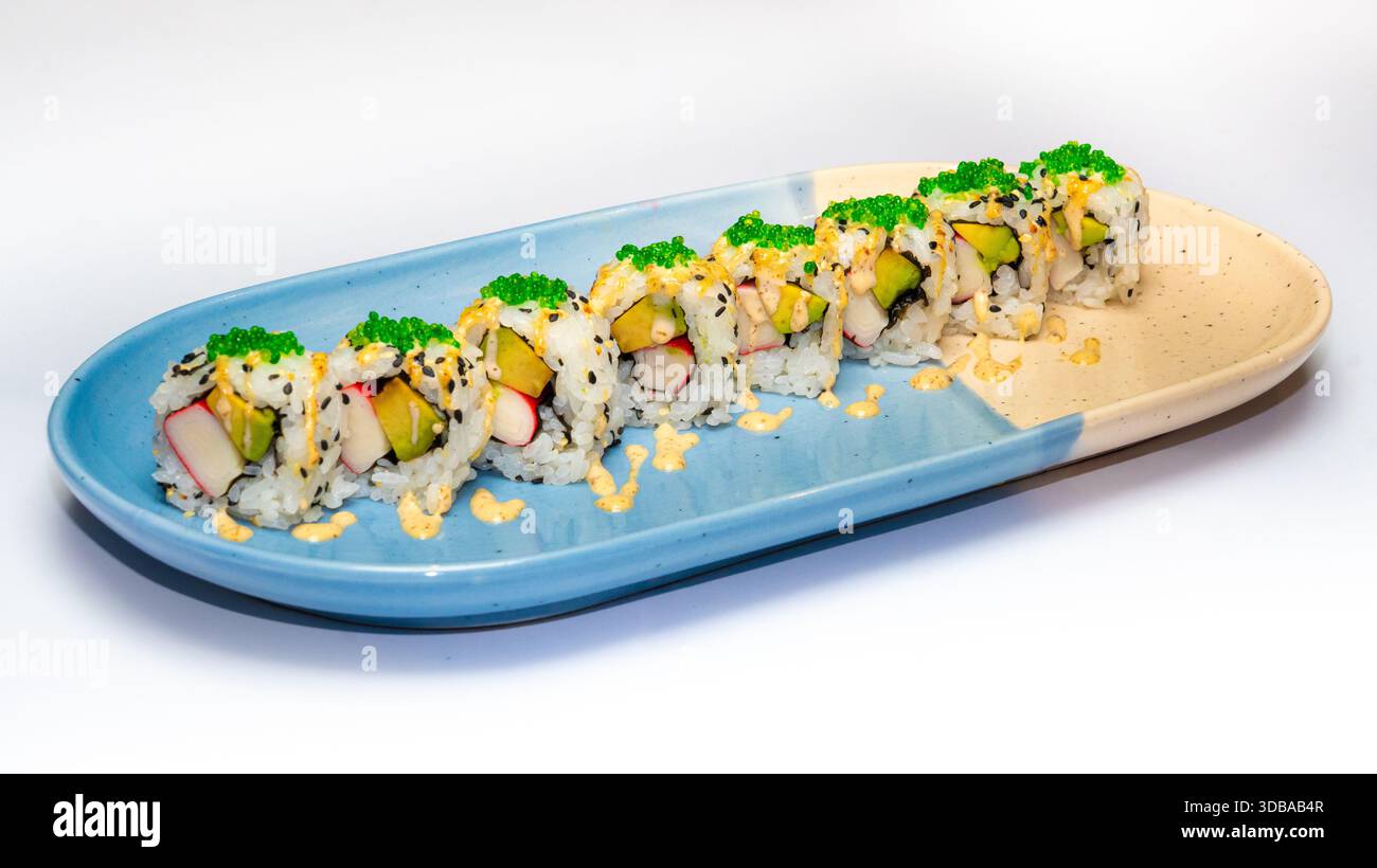 Rouleaux de sushi Uramaki avec avocat, bâtonnets de crabe, tobiko et sauce crémeuse servis sur plaque de céramique isolé sur fond blanc. Banque D'Images