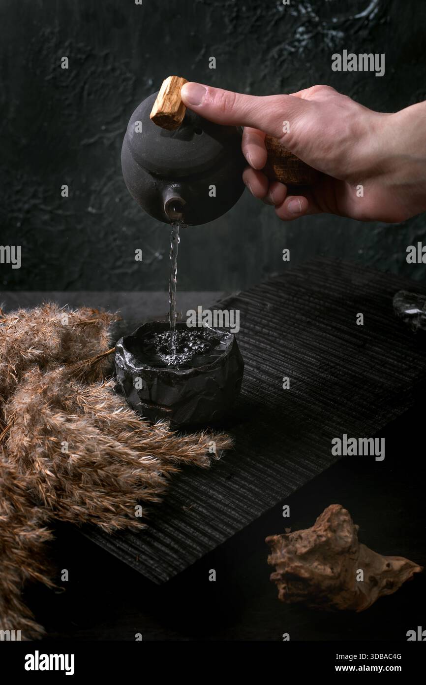 Cérémonie du thé chinois. La main d'un homme verse le thé d'une théière noire traditionnelle en céramique faite à la main avec poignée en bois dans une tasse sur une table de thé sombre. Autum Banque D'Images