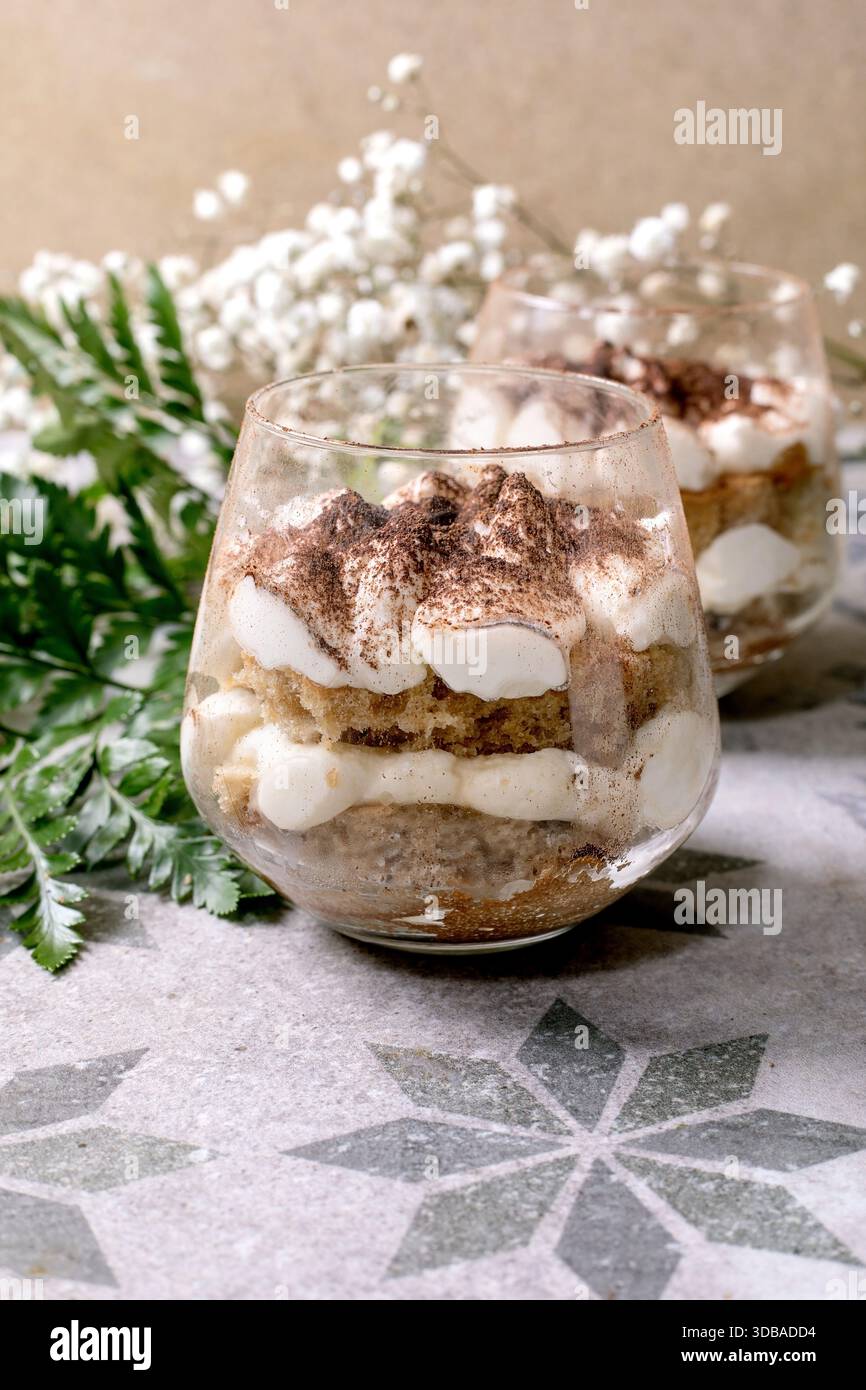 Tiramisu italien classique dans deux verres. Couches de gâteau éponge et crème de mascarpone avec poudre de cacao. Placé sur un carreau à motifs gris-bleu. Bébés blancs Banque D'Images