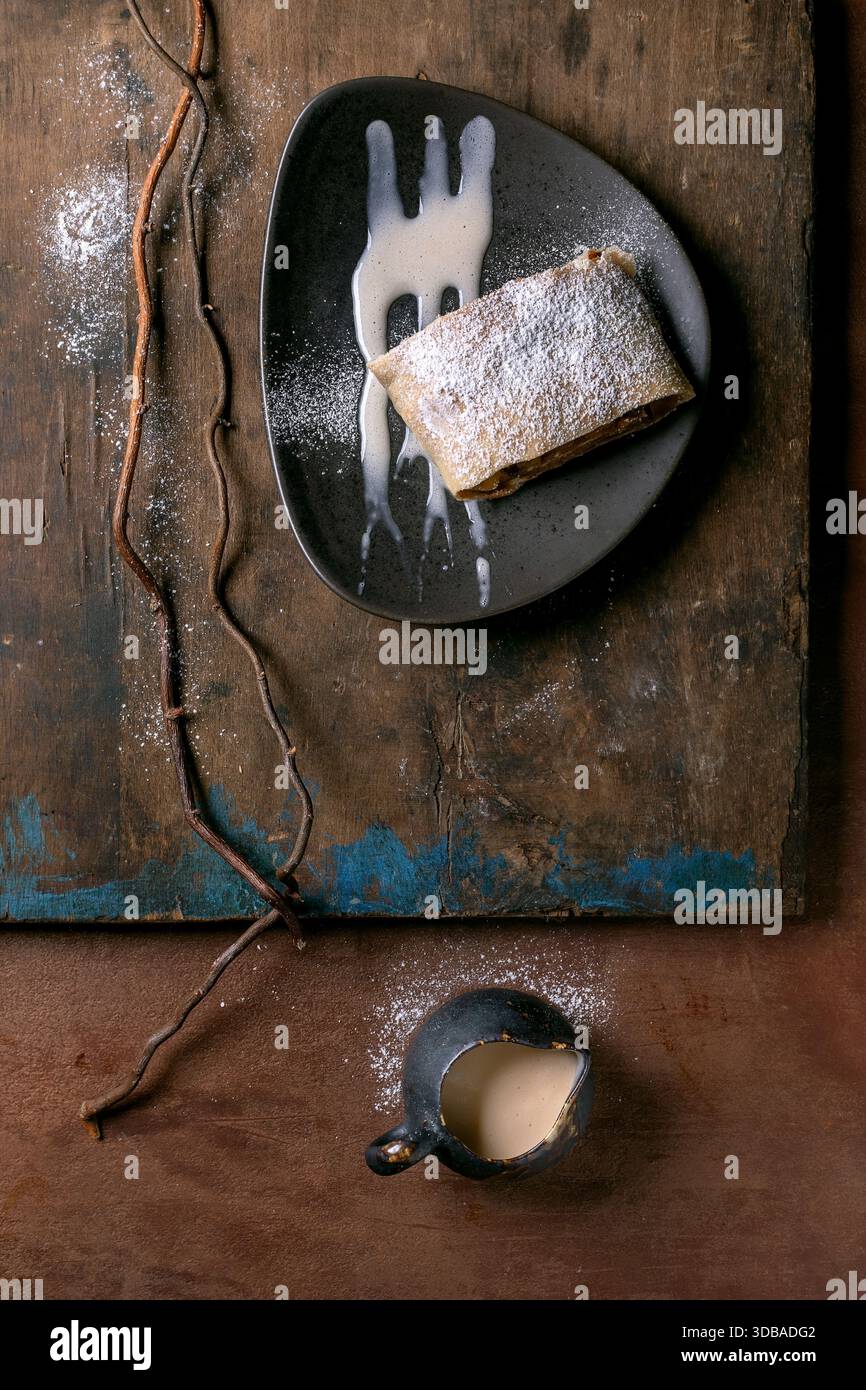 Strudel aux pommes maison traditionnel autrichien avec raisins secs. Nature morte moderne avec struddel de tranche sur plaque en céramique avec sucre en poudre et sauce. Banque D'Images
