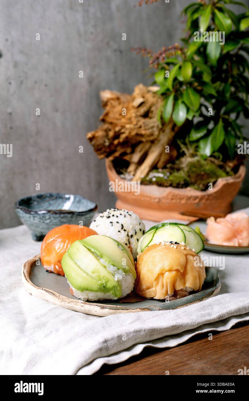 Temari sushi. Boules de sushi tendance avec saumon, avocat, concombre et omelette japonaise sur une assiette wabi-sabi. Sauce soja, gingembre mariné, ikebana sur la table wi Banque D'Images