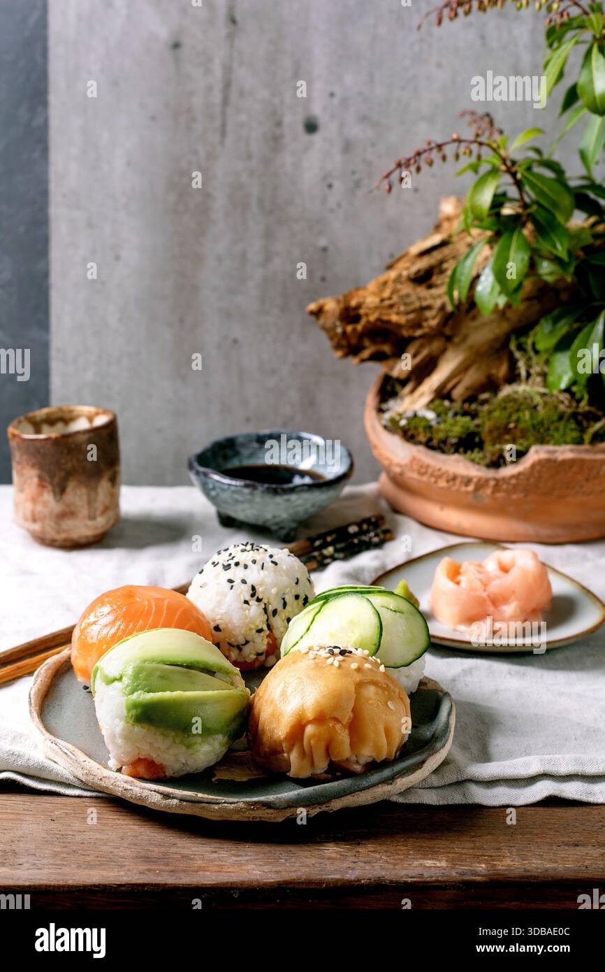 Temari sushi. Boules de sushi tendance avec saumon, avocat, concombre et omelette japonaise sur une assiette wabi-sabi. Sauce soja, gingembre mariné, ikebana sur la table wi Banque D'Images