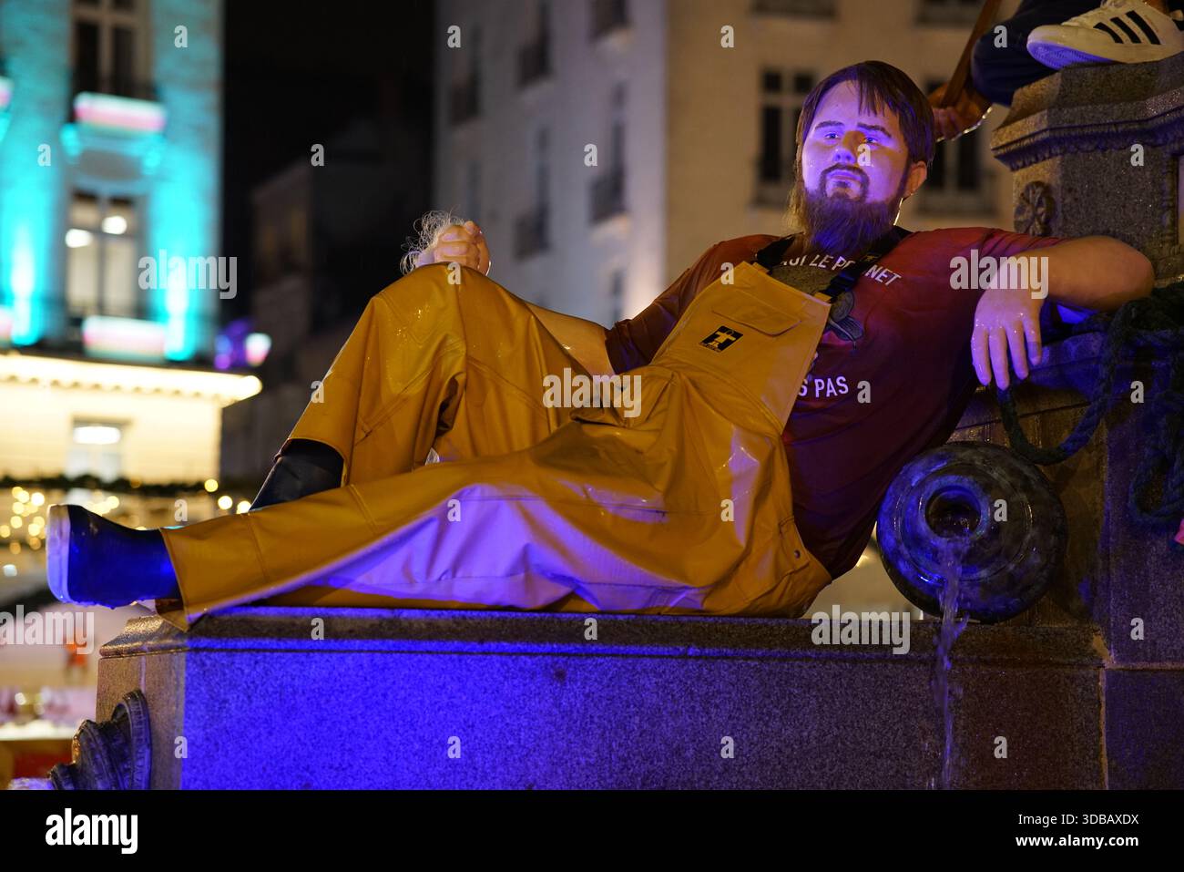 Homme se relaxant sur une structure en pierre la nuit dans le centre-ville de Nantes, France, illuminé par des lumières urbaines.Nantes, France Banque D'Images