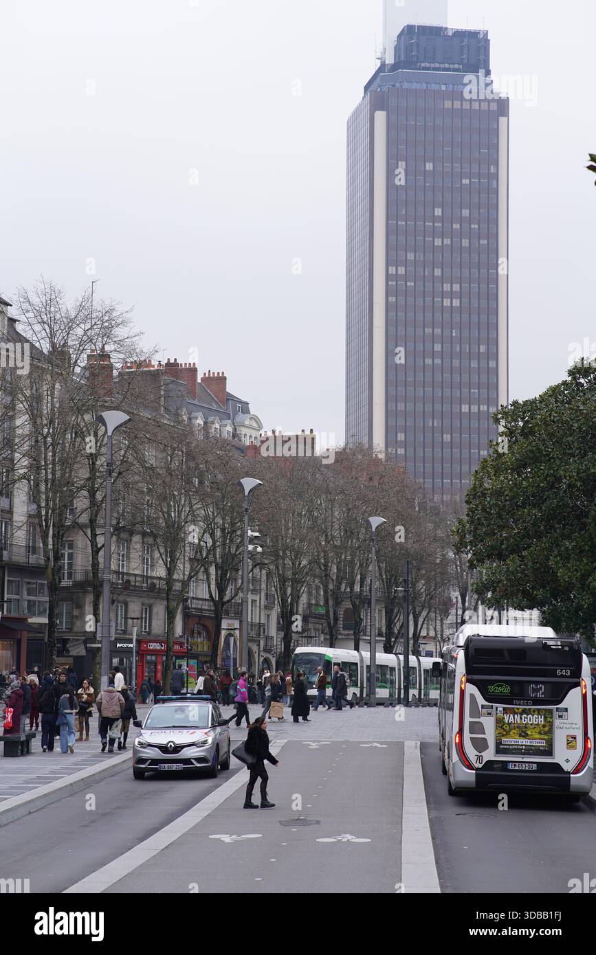 Rue animée de la ville avec des bus, des tramways et des piétons sous une grande tour de grande hauteur sur un jour couvert.Nantes, France Banque D'Images