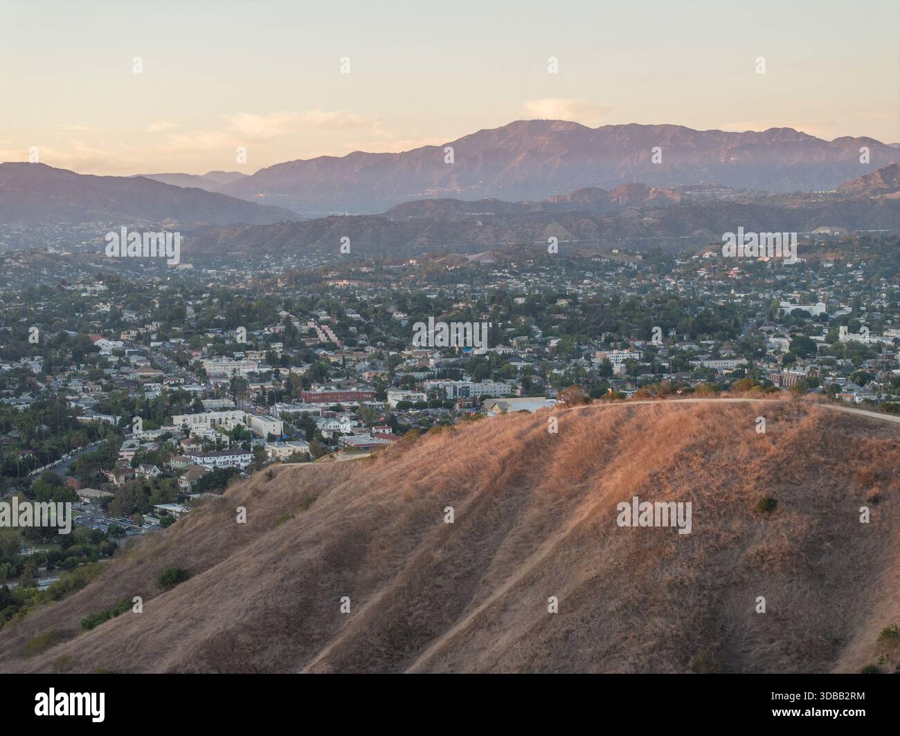 Vue aérienne de la lumière dorée baignant les collines verdoyantes et sèches surplombant le paysage urbain tentaculaire niché au milieu des montagnes lointaines et brumeuses, Los Angeles, Cali Banque D'Images