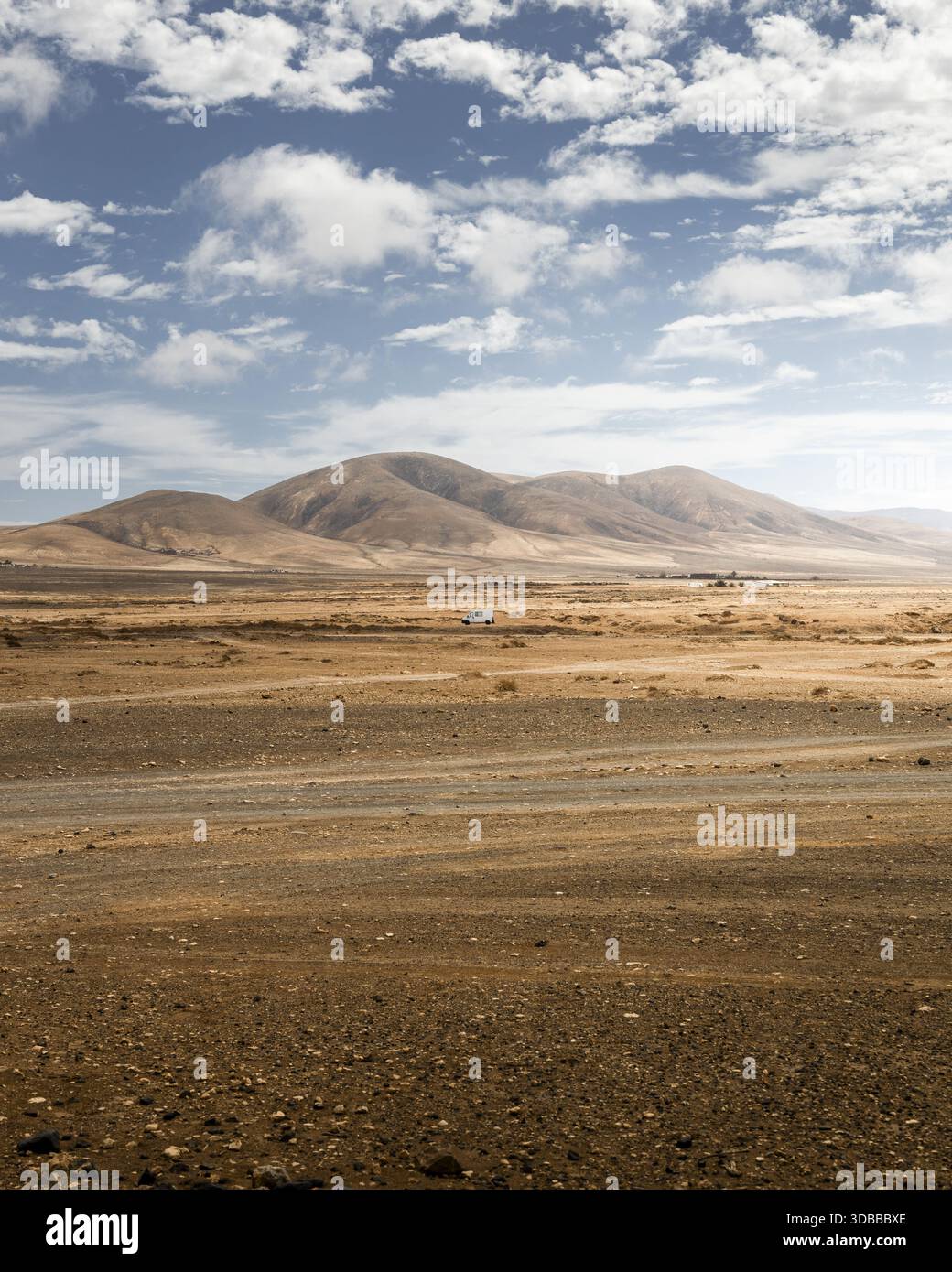 Vue sur le paysage sombre et ensoleillé qui s'étend vers des montagnes lointaines sous un vaste ciel parsemé de nuages, une scène d'une beauté aride, Fuerteventura, Banque D'Images