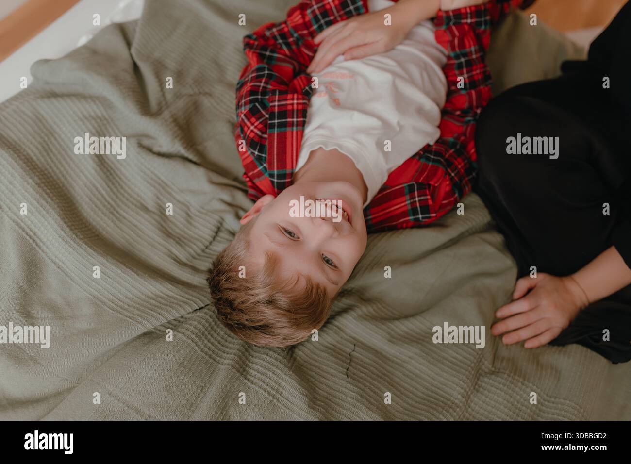 Enfant couché à l'envers portant un pyjama rouge à carreaux dans une chambre douce, moment ludique détendu à la maison. Banque D'Images