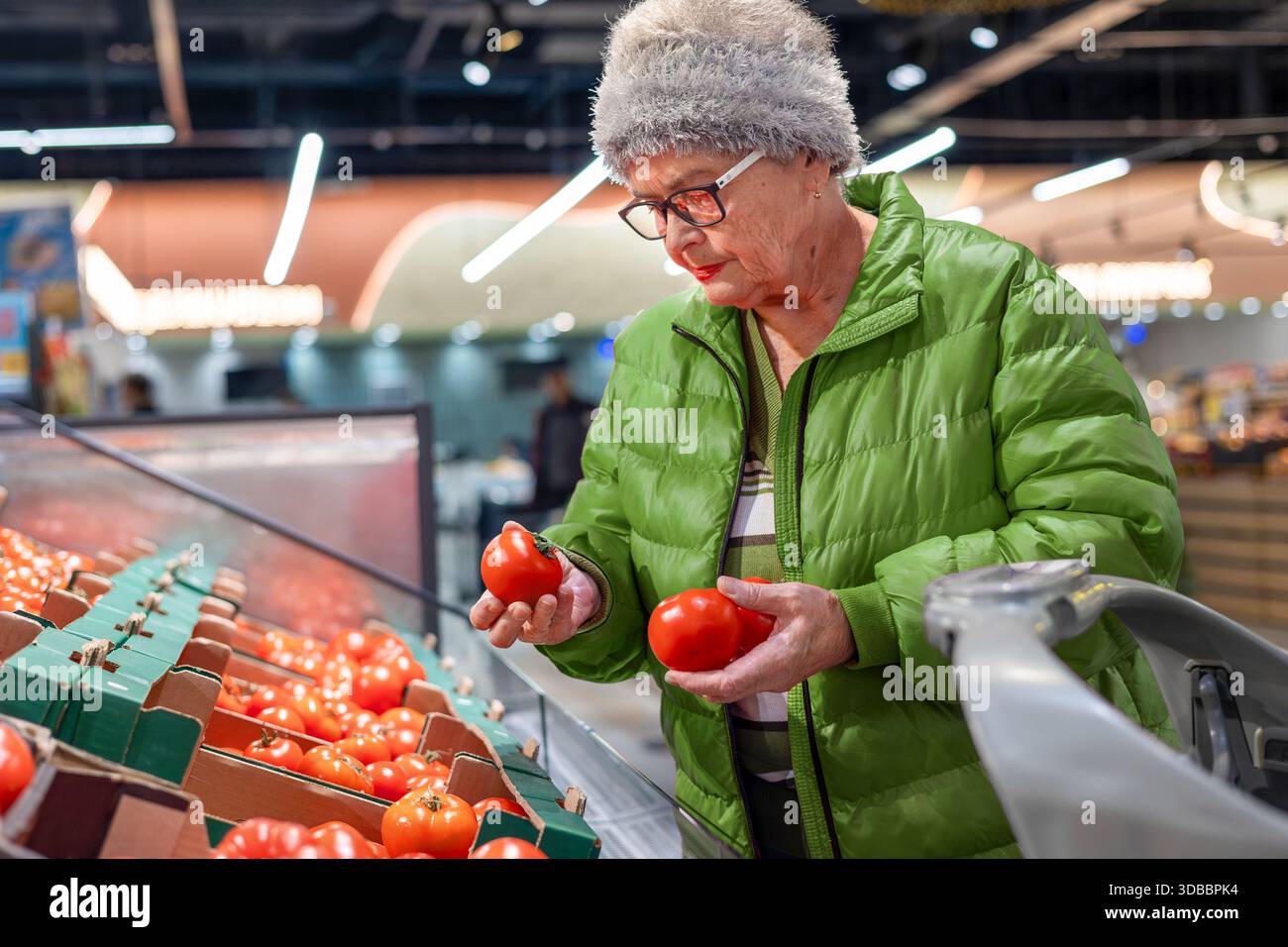 Femme senior comparant et sélectionnant des tomates fraîches dans la section des produits du supermarché moderne. alimentation saine, sélection d'aliments frais, aîné indépendant Banque D'Images