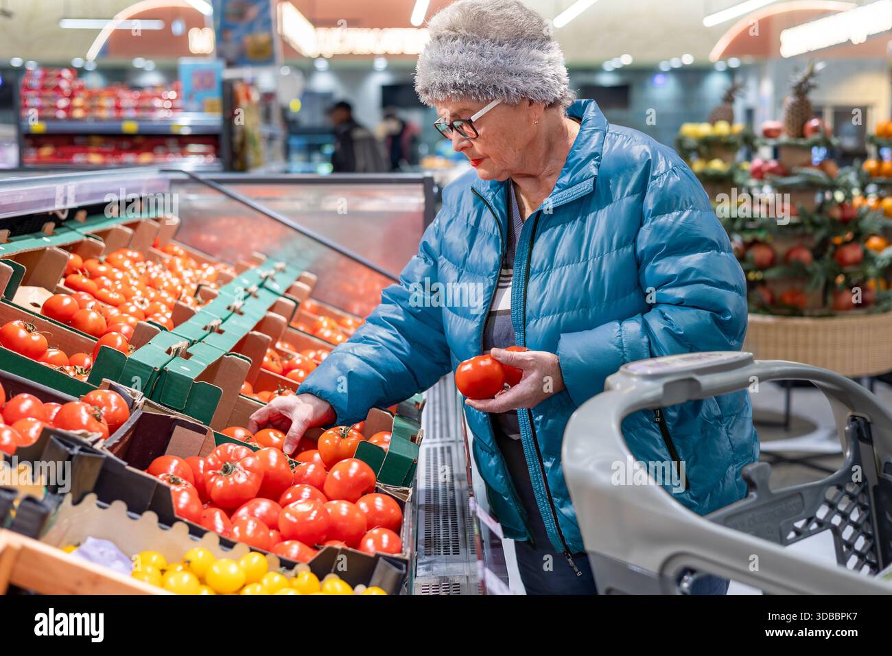 Femme senior comparant et sélectionnant des tomates fraîches dans la section des produits du supermarché moderne. alimentation saine, sélection d'aliments frais, aîné indépendant Banque D'Images
