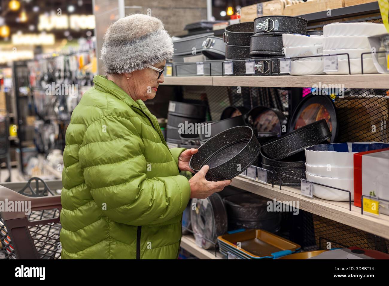 Femme âgée choisissant la plaque de cuisson dans la section articles ménagers de supermarché, comparant les prix des ustensiles de cuisine, mode de vie senior actif, achats indépendants, Banque D'Images