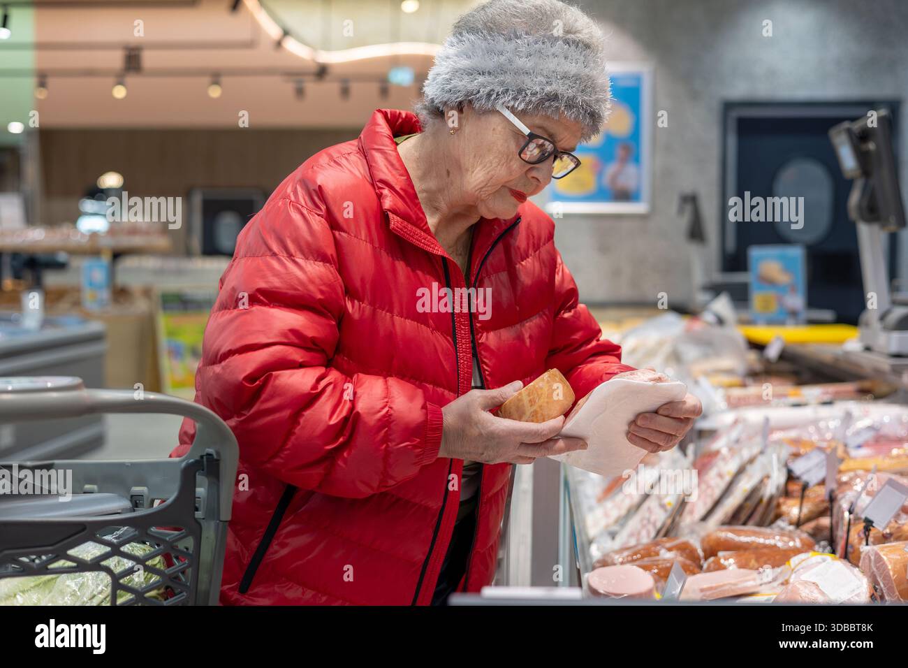 Femme senior lisant l'étiquette du produit tout en achetant de la viande de charcuterie dans la section réfrigérée du supermarché.Smart Senior Consumer : femme âgée budget Banque D'Images