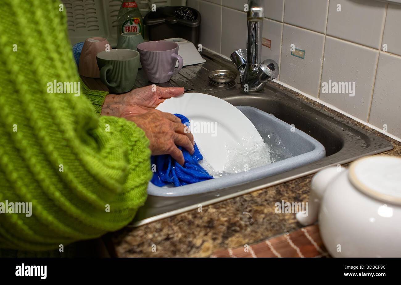 Personne âgée lavant la vaisselle à la main dans un évier, une corvée domestique commune dans un cadre de cuisine typique Banque D'Images