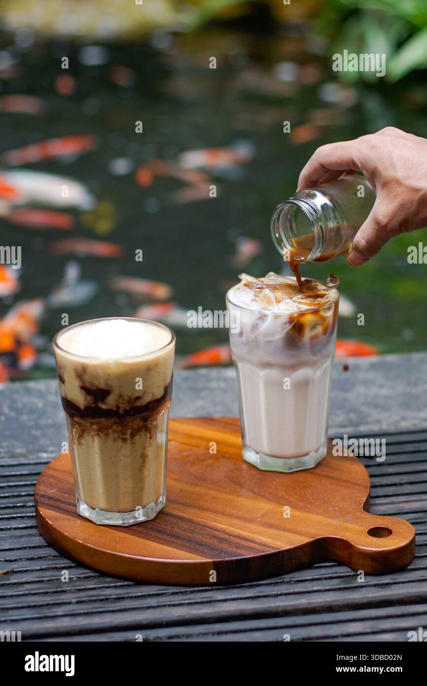 Café glacé et latte glacé servis sur planche de bois, sirop de café versé, ambiance café en plein air Banque D'Images