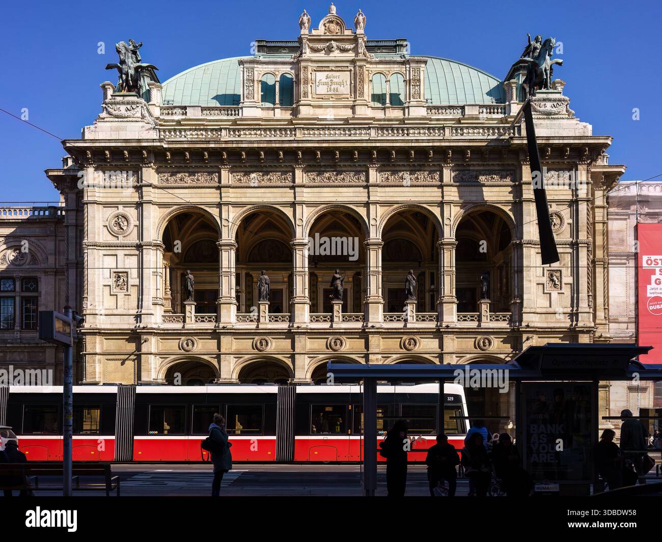 Vienne, Autriche - 3 octobre 2025 - tramway rouge passant devant l'Opéra national de Wien avec des gens debout à l'arrêt. Banque D'Images