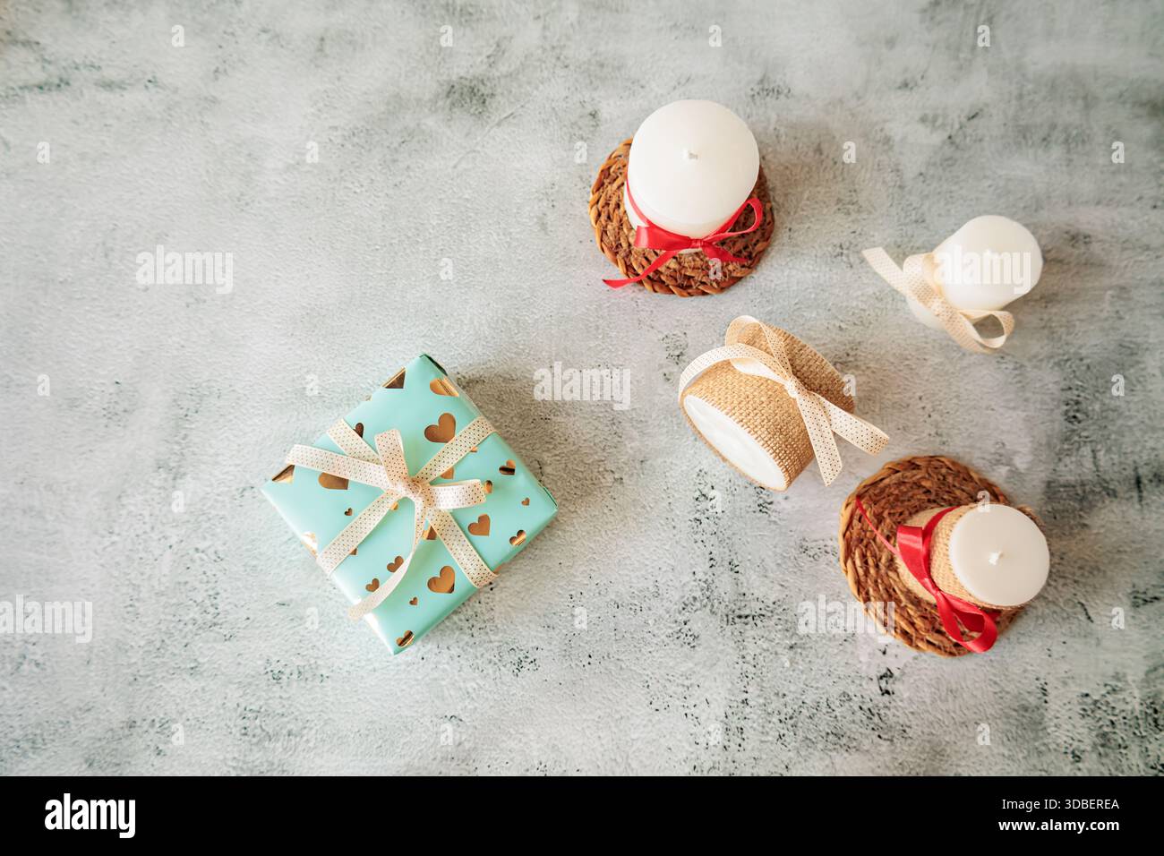 Pose plate avec des bougies rustiques et une boîte cadeau magnifiquement emballée en papier turquoise avec des coeurs dorés. Parfait pour un design de vacances saisonnier ou romantique Banque D'Images