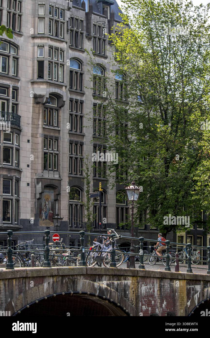 Vue sur un pont animé avec cyclistes et piétons, encadré par des bâtiments historiques et des arbres verdoyants, créant une scène urbaine dynamique, Amsterdam, Banque D'Images