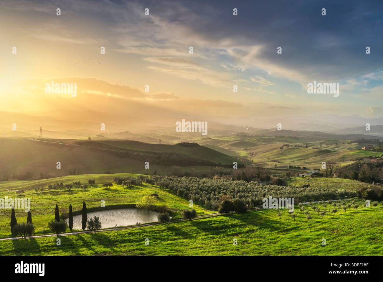Vue panoramique sur la campagne emblématique de Volterra, Toscane, Italie au lever du soleil. Comprend des collines vallonnées, des oliveraies et un étang, avec un throu de lumière dorée Banque D'Images