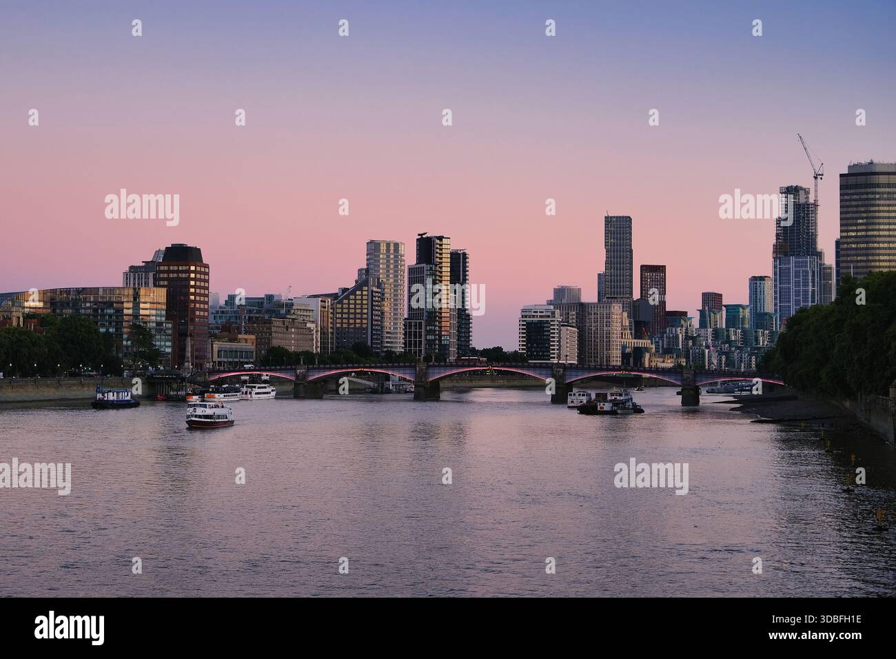 Panorama crépusculaire des gratte-ciel de Londres sur la Tamise avec pont illuminé et bateaux reflétant le ciel rose violet couché de soleil sur les gratte-ciel modernes Banque D'Images