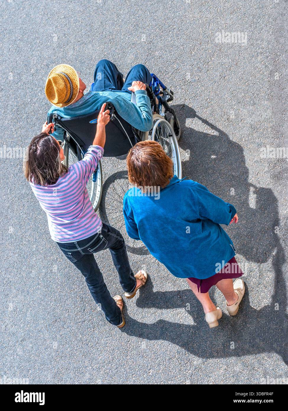 Vue aérienne de deux femmes aides poussant un homme plus âgé invalide dans un fauteuil roulant - centre de la France. Banque D'Images