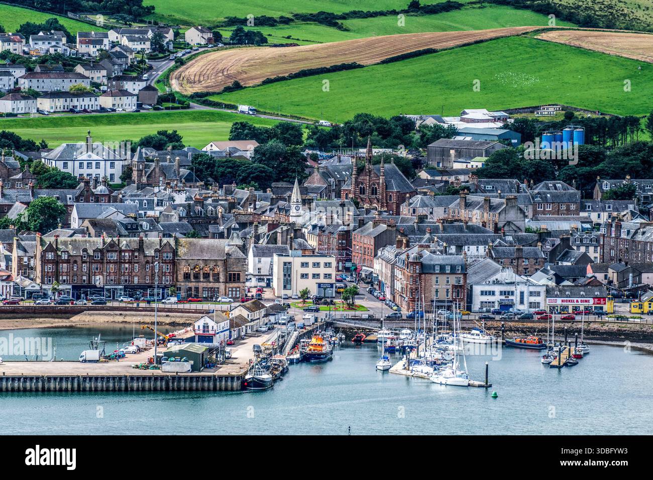 Un pittoresque paysage côtier avec le port de Campbeltown rempli de bateaux, de bâtiments historiques en pierre et de collines verdoyantes en arrière-plan Banque D'Images