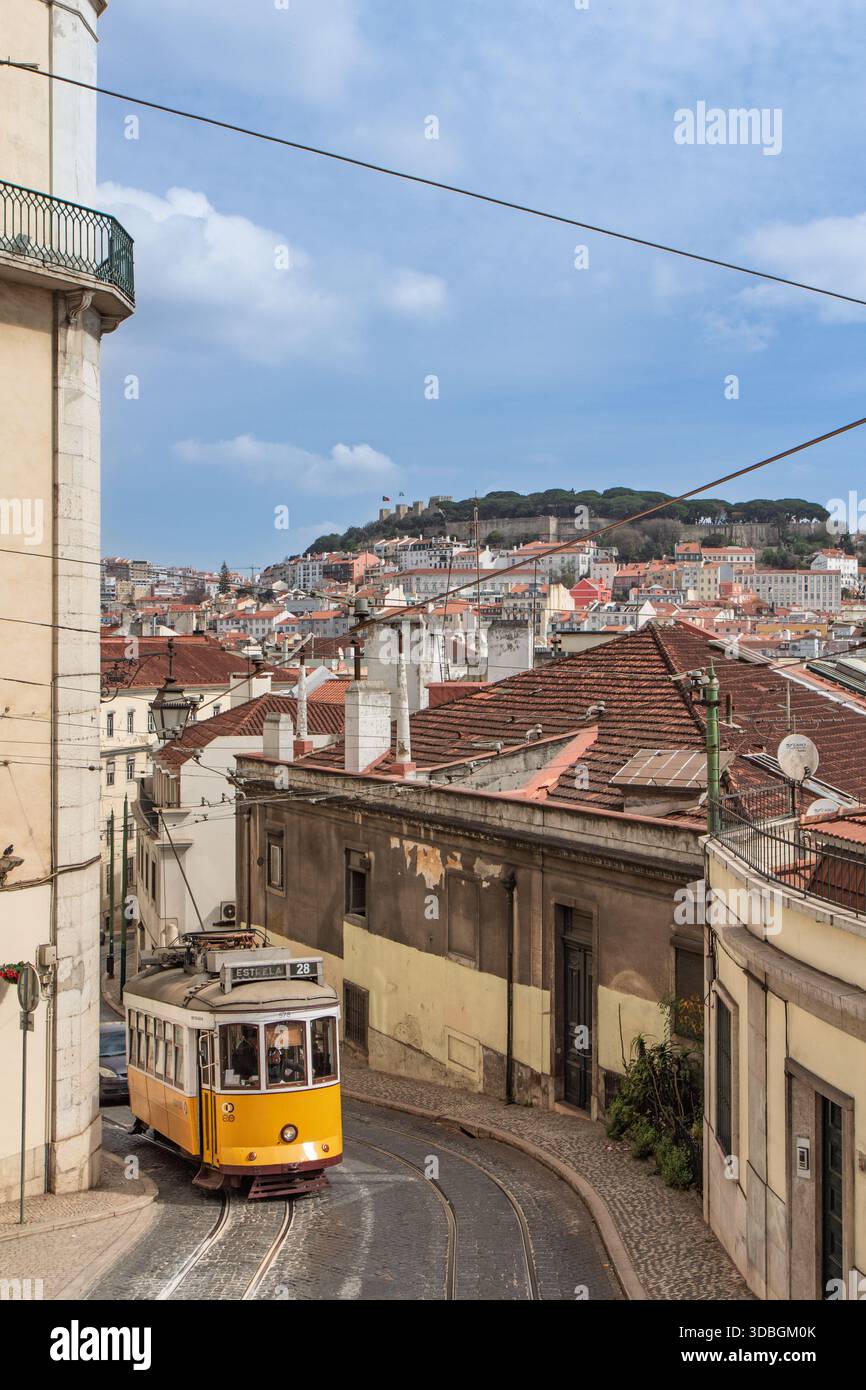 L'emblématique Tram 28 jaune serpentant à travers les rues de Lisbonne avec l'historique Castelo de São Jorge visible sur la colline en arrière-plan. Banque D'Images