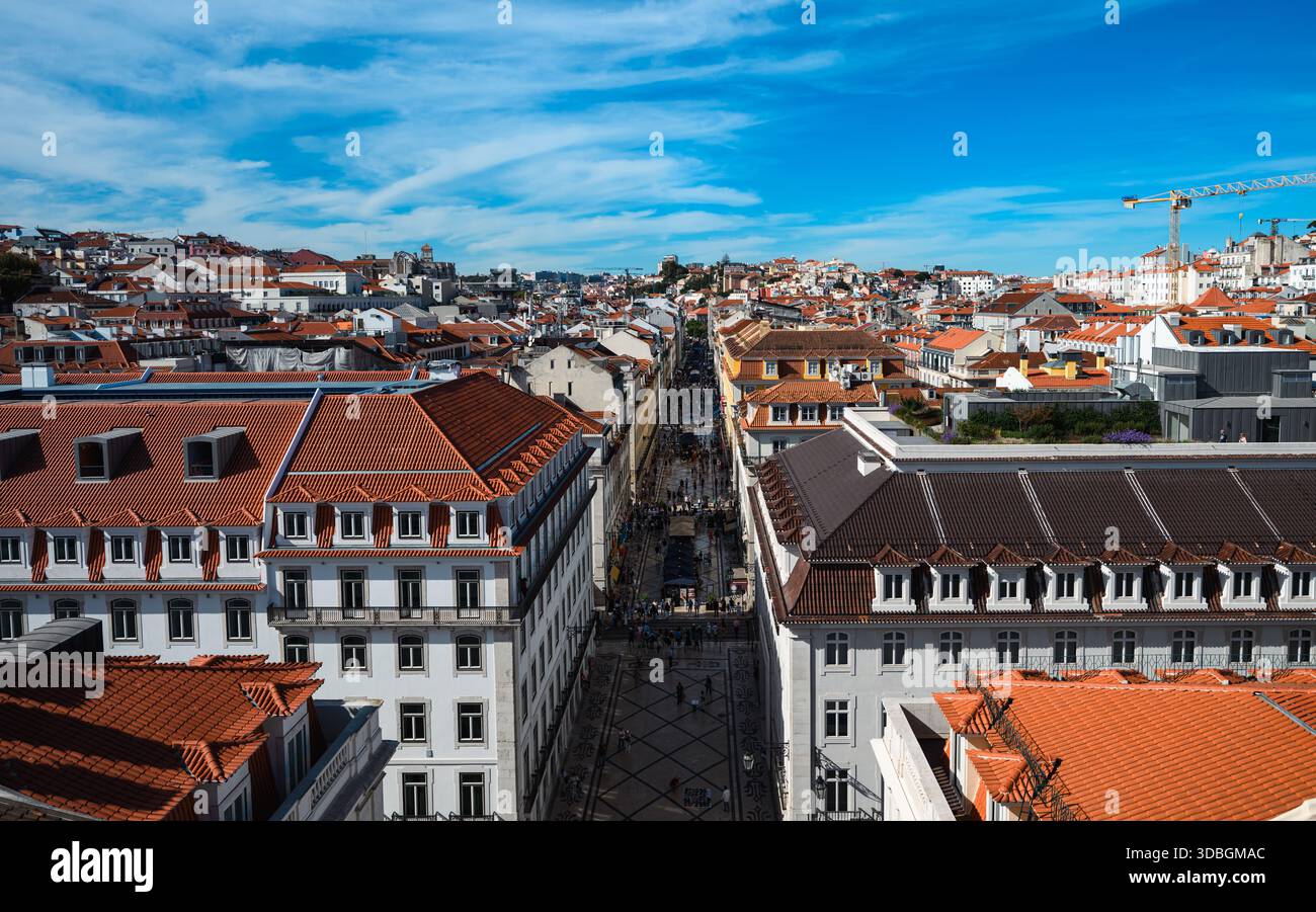 Vue panoramique sur la vieille ville de Lisbonne avec des toits traditionnels en tuiles rouges et une longue rue piétonne qui s'étend à travers le centre-ville historique. Banque D'Images