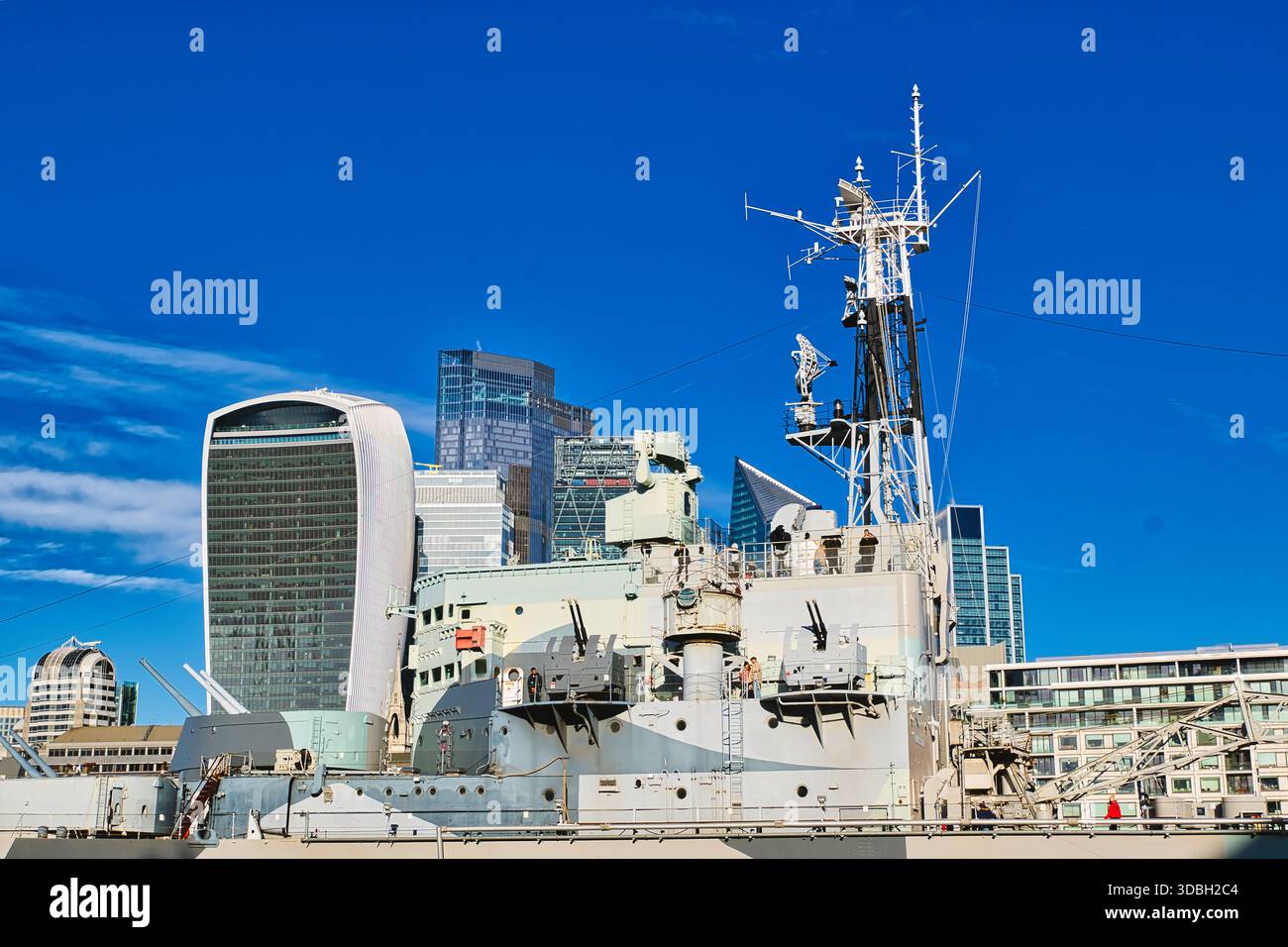 Le pont et la superstructure d'un navire de guerre gris sont proéminents sur fond de gratte-ciel londoniens modernes sous Un ciel bleu clair. Les armes du navire et Banque D'Images