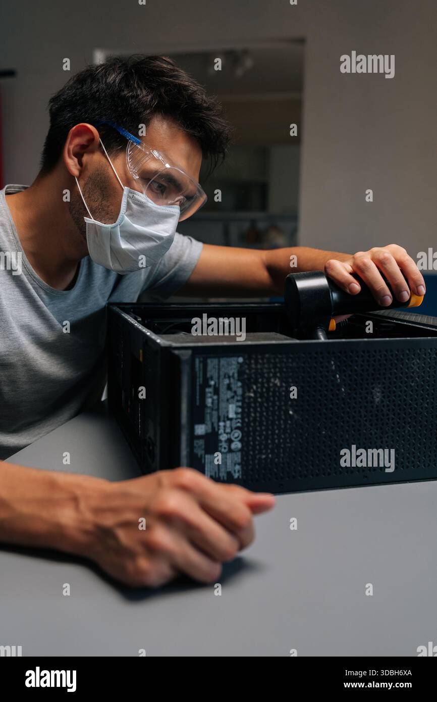 Portrait vertical de technicien informatique dans le masque de protection et l'unité de système de nettoyage de lunettes de sécurité avec vide pendant la maintenance matérielle de précision. Banque D'Images