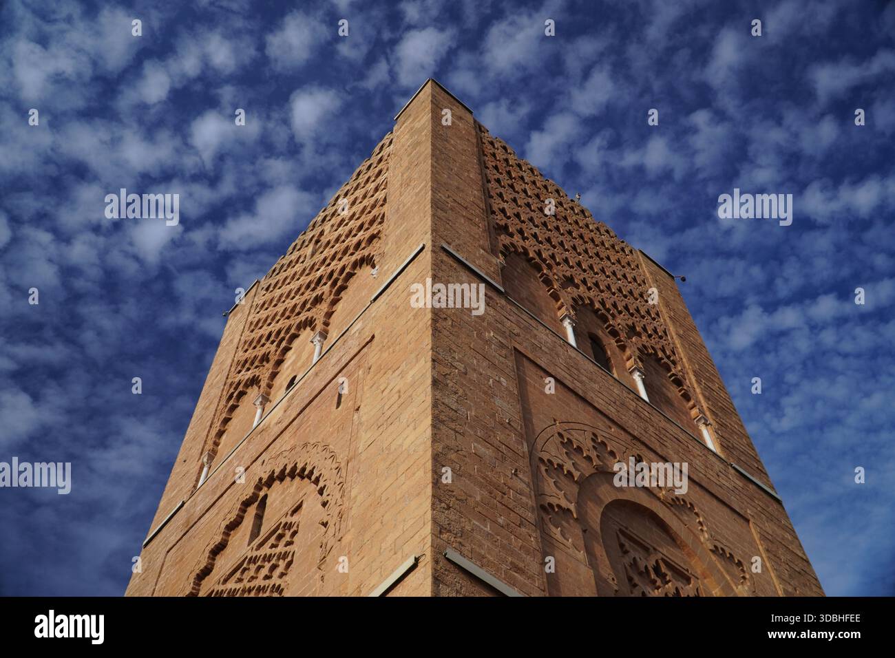 Tour Hassan sous un ciel parsemé de petits nuages. La vue d'en bas met en évidence les détails architecturaux fins. Banque D'Images