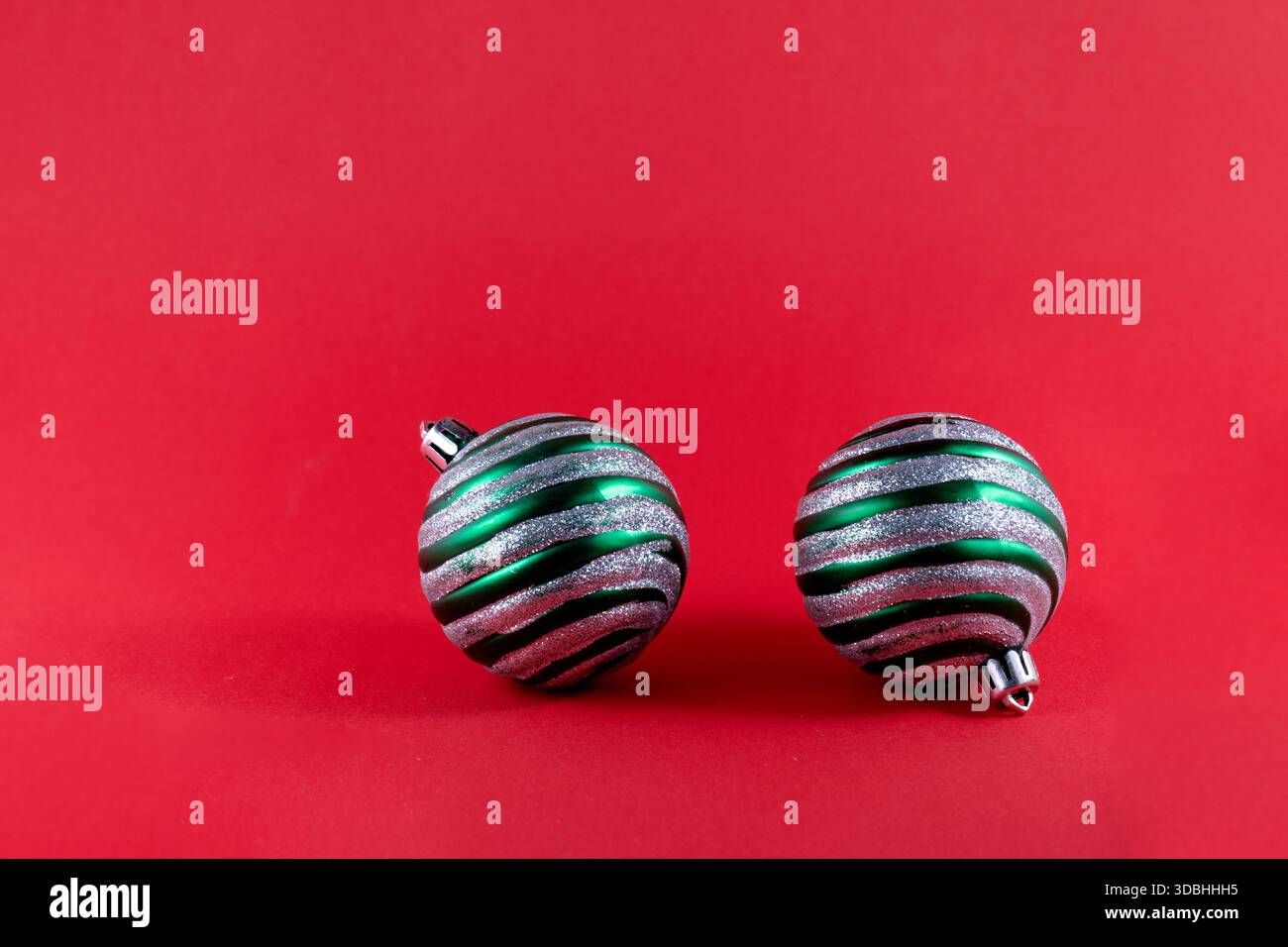 Deux ornements de Noël rayés dans des tons verts et gris affichés sur un fond rouge. Le design allie tradition et modernité, parfait pour fe Banque D'Images