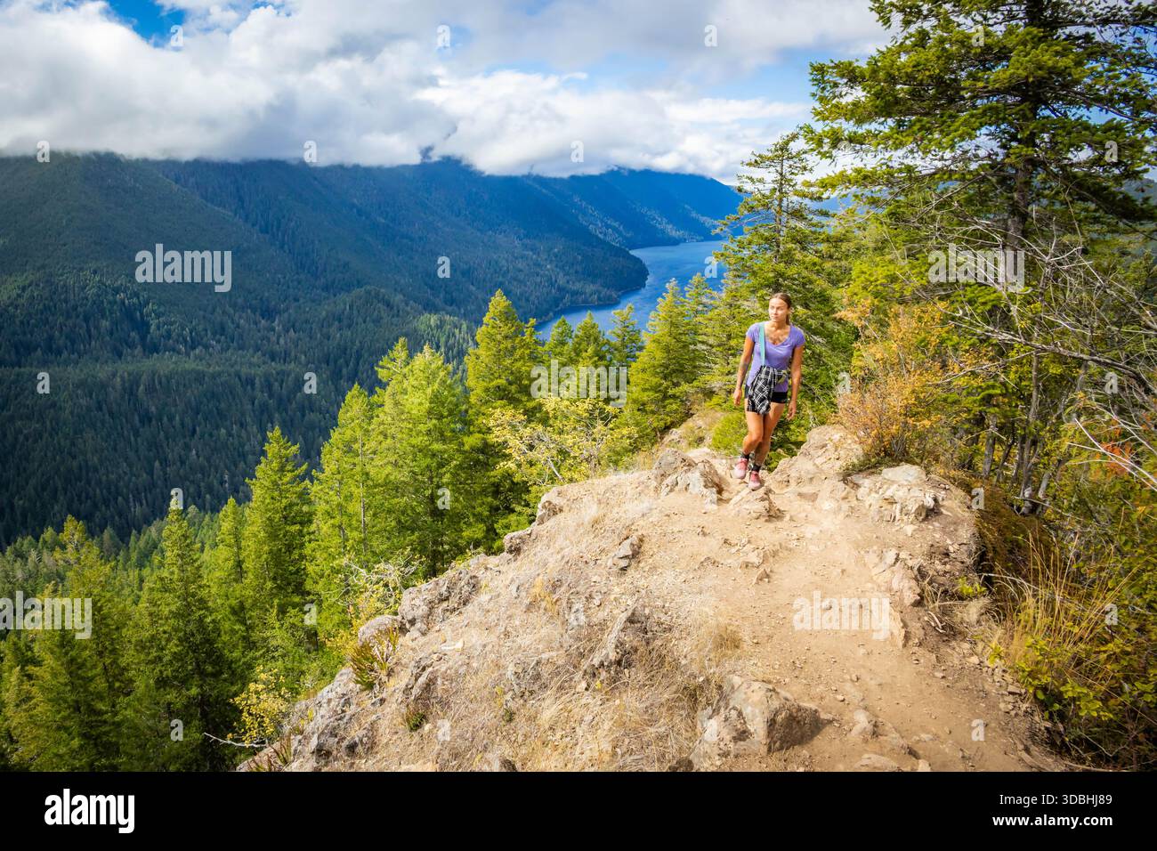 Une femme randonneuse heureuse est capturée lors de son ascension acharnée, marchant activement vers le sommet difficile du mont Storm King dans le parc national olympique. Banque D'Images