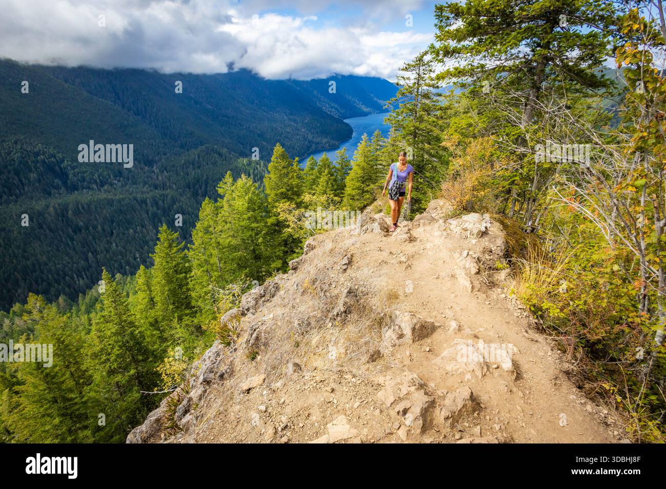 Une femme randonneuse heureuse est capturée lors de son ascension acharnée, marchant activement vers le sommet difficile du mont Storm King dans le parc national olympique. Banque D'Images