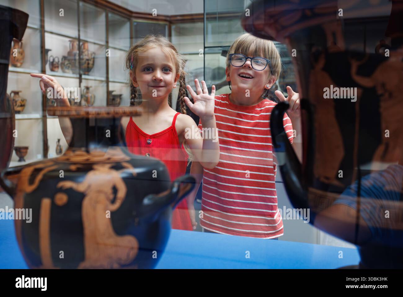 Fille et garçon excités dans le musée vague mains à travers la vitrine de verre Banque D'Images