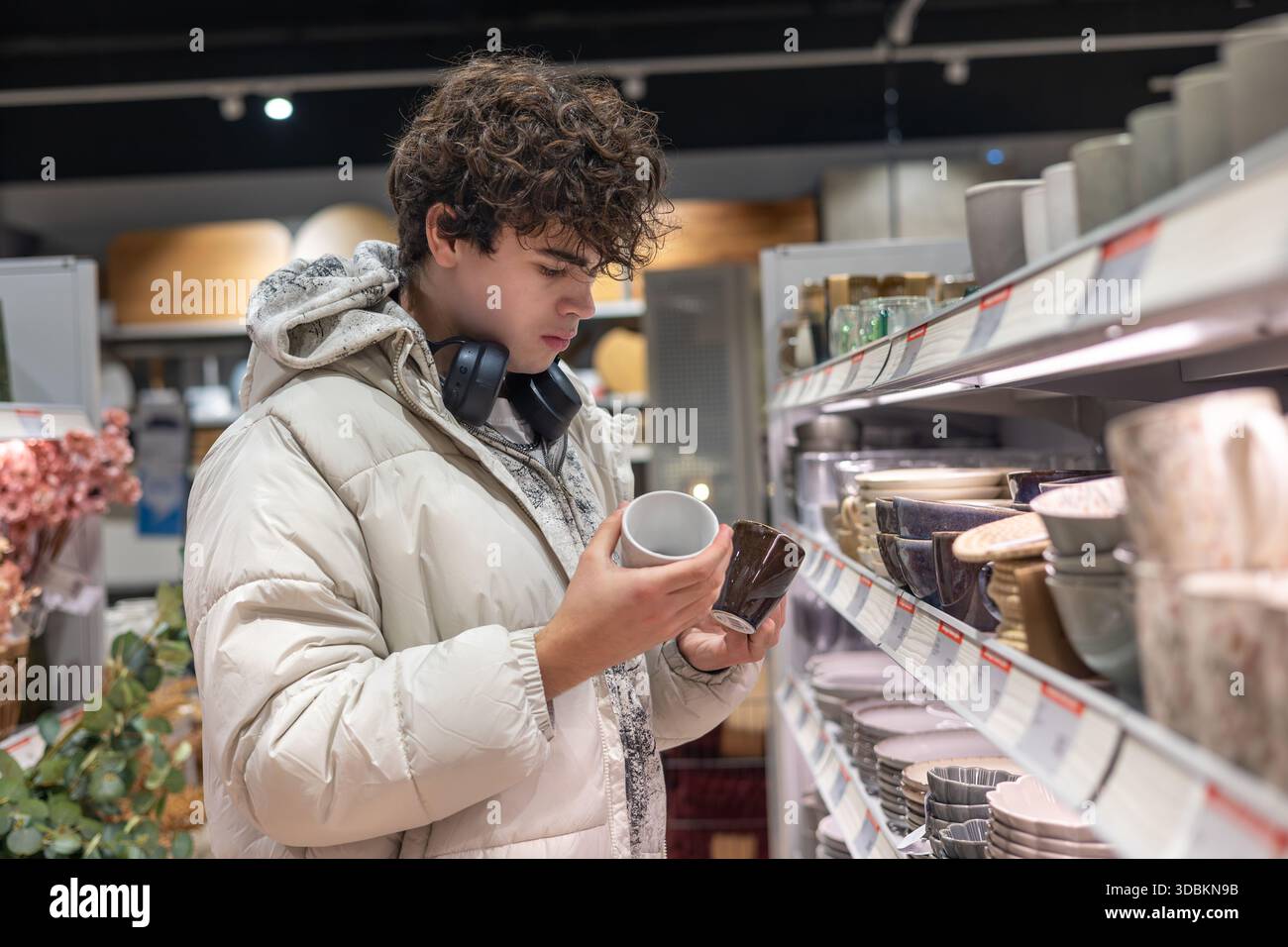 Adolescent comparant les tasses dans l'allée des ustensiles de cuisine – jeune client choisissant des tasses en céramique dans le magasin d'articles ménagers. Banque D'Images