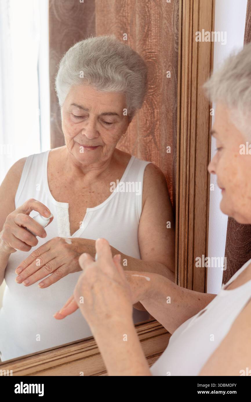 Femme âgée appliquant la crème pour les mains et massant ses mains devant le miroir – soins de la peau, soins personnels et routine beauté pour la peau mature. Banque D'Images