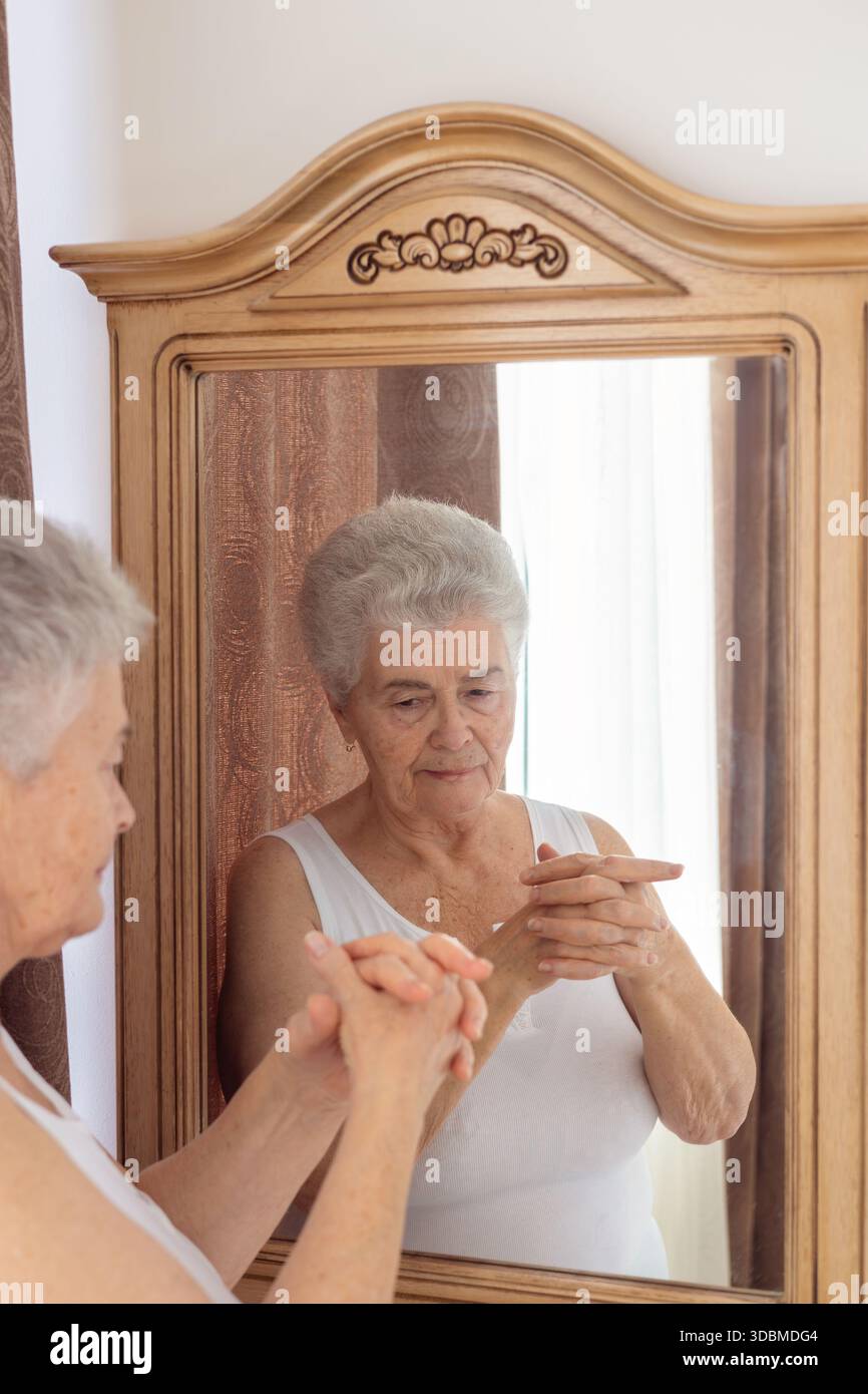 Femme âgée appliquant la crème pour les mains et massant ses mains devant le miroir – soins de la peau, soins personnels et routine beauté pour la peau mature. Banque D'Images