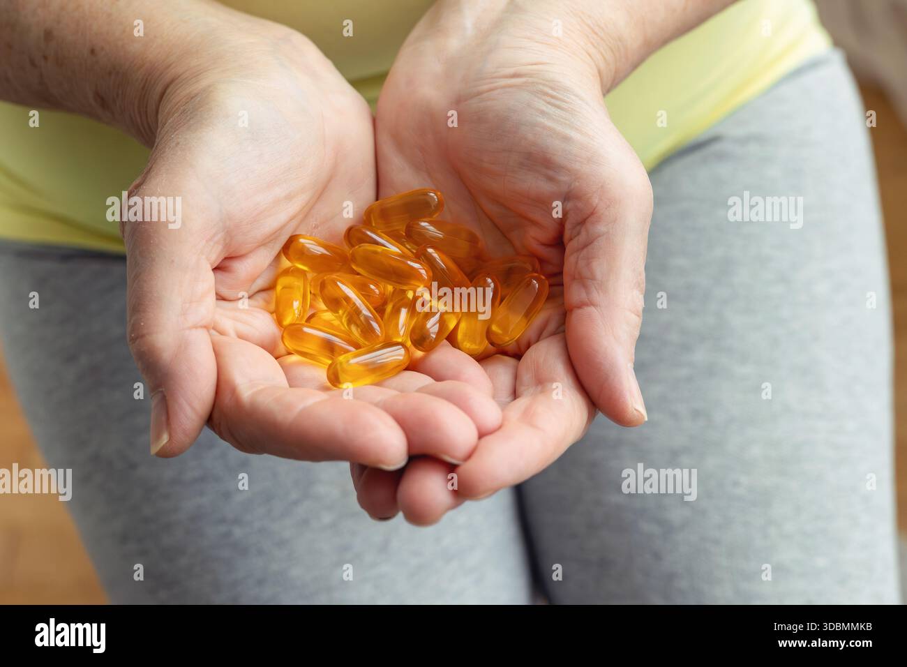 Mains vieillissantes tenant des capsules dorées. Santé à l'âge adulte, maintien de l'activité et de l'énergie. Prévention des maladies, utilisation de vitamines et de suppléments, traitement Banque D'Images