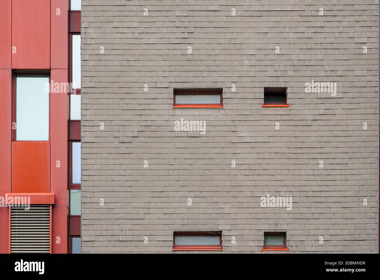 Zurich, Suisse, façade d'un bâtiment industriel-commercial combinant des carreaux de briques grises sourdes avec des panneaux verticaux rouges audacieux, ponctués de petites fenêtres étroites avec des appuis rouges. Banque D'Images