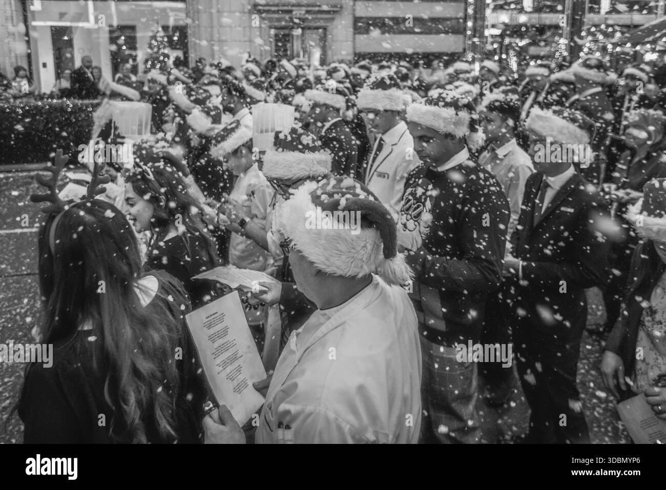 Image en noir et blanc de chanteurs de medley de Noël dans la neige au Savoy Hotel à Londres. Banque D'Images