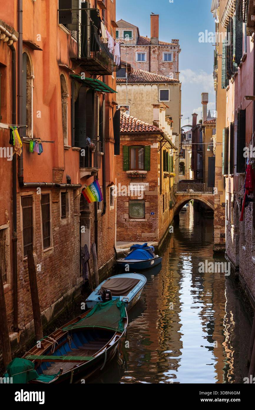 Canal tranquille avec maisons en stuc colorées et balcons en métal donnant sur l'eau. Canots à moteur amarrés le long d'une entrée. Lessive suspendue à des lignes à l'extérieur des fenêtres, et un drapeau de la paix, rythme, flottant à partir d'une fenêtre reflétant l'inquiétude autour de la guerre contre l'Ukraine. Banque D'Images