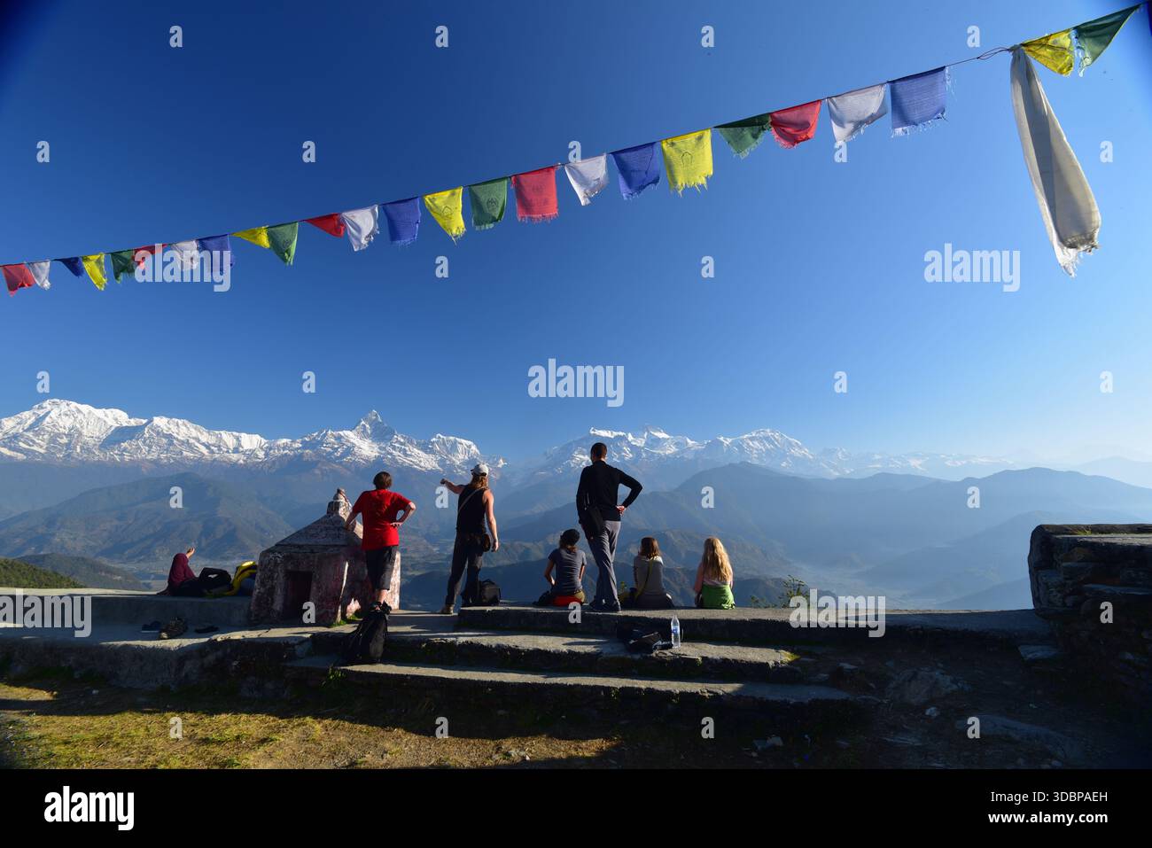 Touristes à un point de vue surplombant la chaîne de montagnes Annapurna dans l'Himalaya, Népal, avec des drapeaux de prière colorés au-dessus et une vue large sur la montagne. Banque D'Images