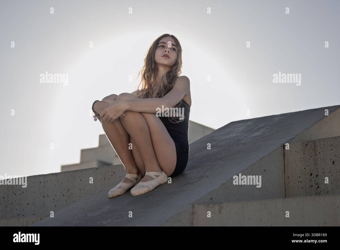 Réfléchie fille de 12 ans assis sur une structure en béton moderne à l'extérieur pendant l'heure d'or Banque D'Images