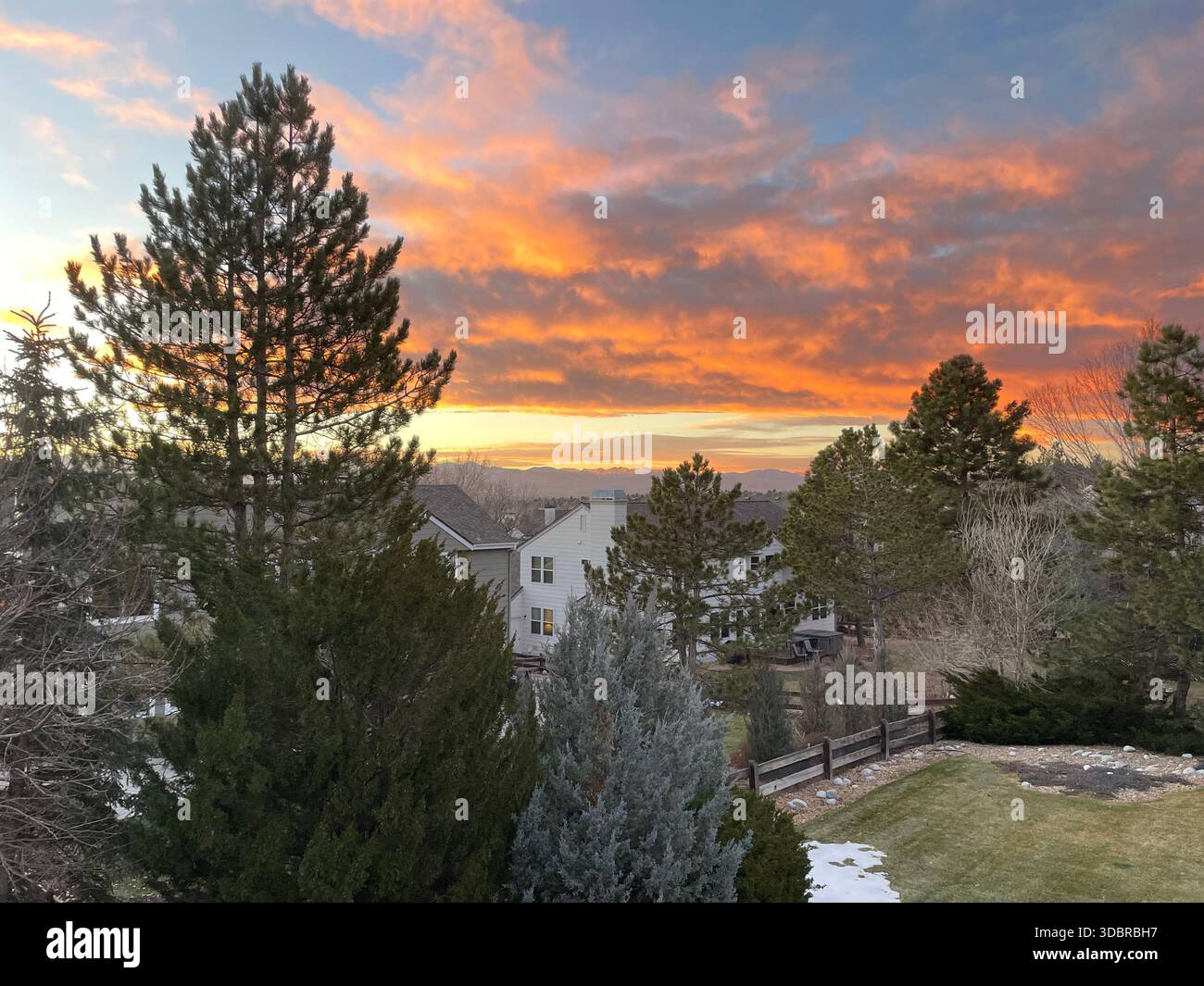 Les teintes dorées se fondent dans le crépuscule tandis qu'un quartier calme se niche sous les arbres poussiéreux de neige et les montagnes majestueuses. - Image de stock capturée avec un smartphone