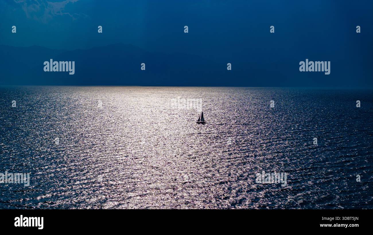 Un voilier solitaire dérivant à travers les eaux chatoyantes du lac Fuxian au coucher du soleil, avec une lumière spectaculaire se reflétant sur l'eau calme Banque D'Images